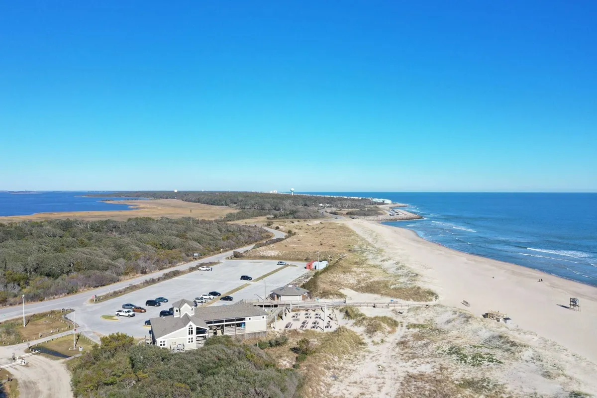 This exterior image captures a relaxing beachfront scene, complete with a parking area, a restaurant in view, and sweeping ocean vistas. The inviting setting hints at the proximity to local dining, the bustle of the boardwalk, and ample space for groups to gather by the shore.