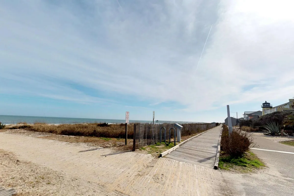 A wooden boardwalk winds through dune grass toward a stunning ocean view. The scene captures the anticipation of reaching the beach and the natural beauty that surrounds the property.