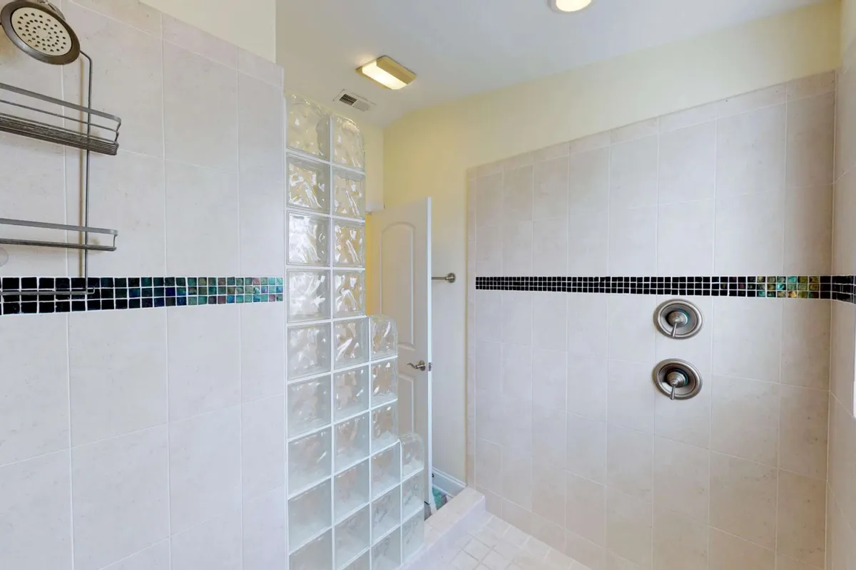A stylish bathroom interior featuring a glass block shower wall, dark mosaic tile accents, and modern fixtures. The scene feels fresh and serene, ideal for rinsing off after a day at the beach.