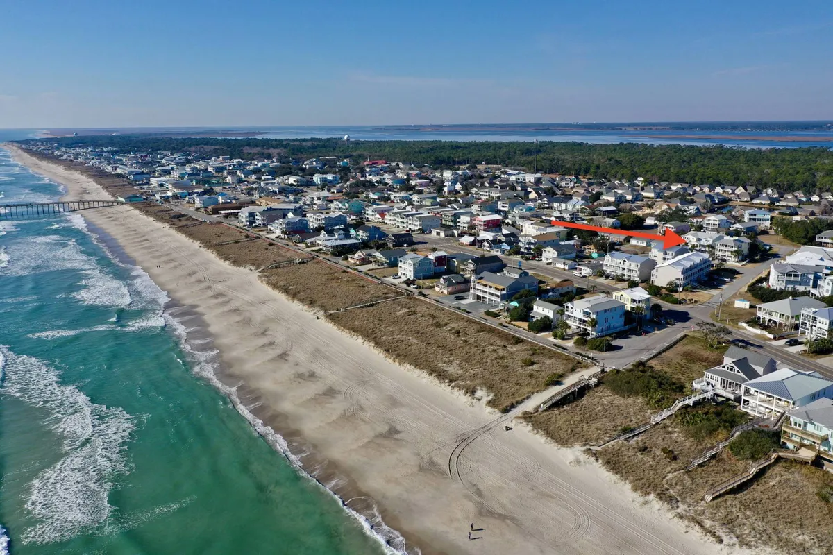 This image features a picturesque beach scene with a pier extending over the ocean, bordered by nearby houses. The setting is ideal for beach walks, enjoying nature, and spending time with pets. The tranquil atmosphere and open space evoke the freedom of seaside living.