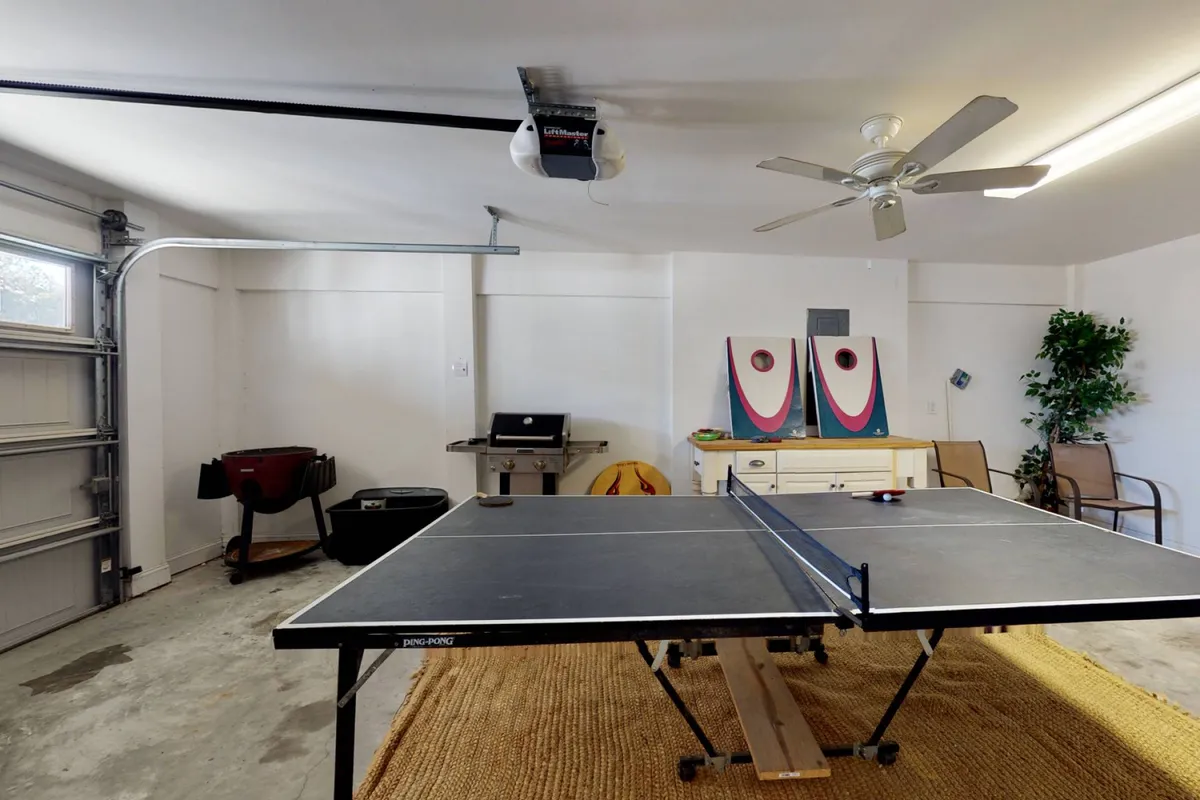 A bright and energetic game area featuring a modern ping pong table, lively artwork on the wall, a green plant adding a touch of nature, and comfortable furniture arranged for relaxation or socializing. The space is open and inviting, ideal for friendly competition and family gatherings.