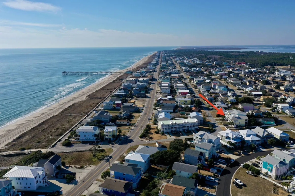 A broad view encompassing the beach, pier, nearby houses, and a road leading toward local shops. The image portrays a tranquil atmosphere with the beach and pier as focal points, inviting guests to explore vibrant local life, morning coffee rituals, and various events.