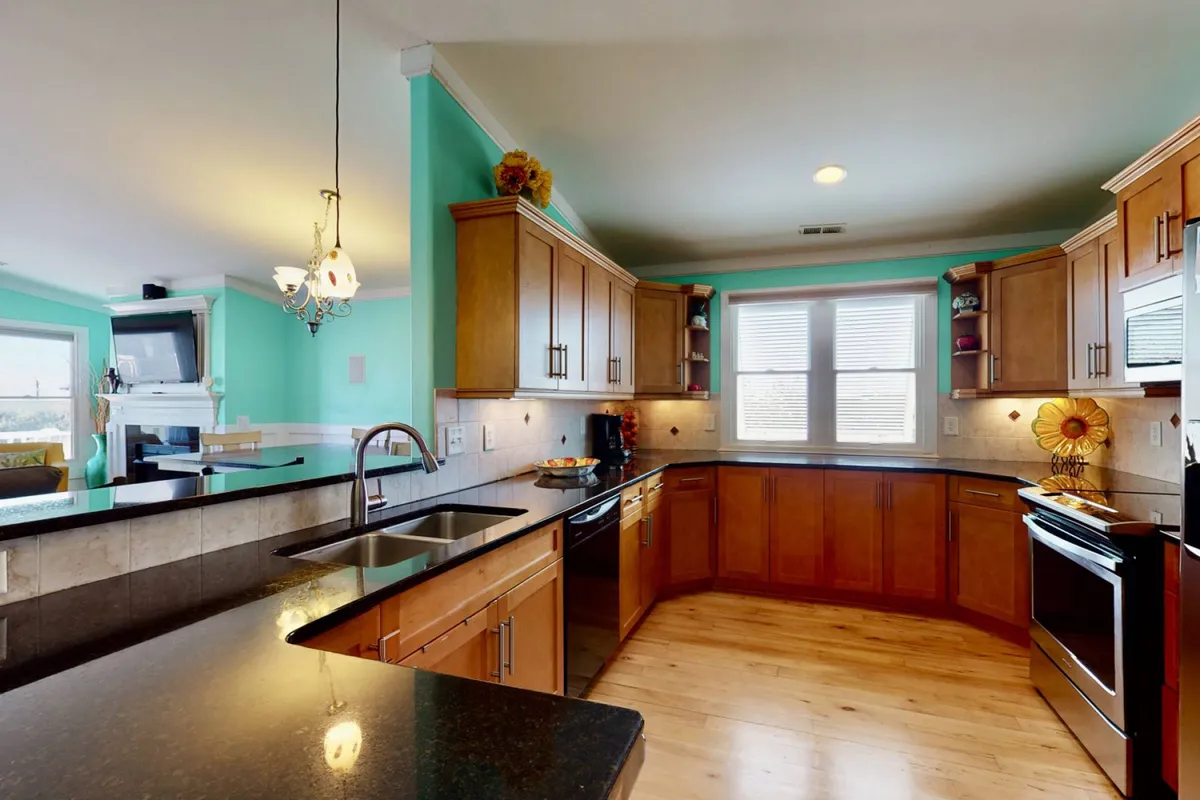 A vibrant, well-lit kitchen with stylish cabinetry, black countertops, modern appliances, and windows that bathe the space in sunlight. The layout encourages easy movement and interaction, making it perfect for cooking, entertaining, or casual family breakfasts.